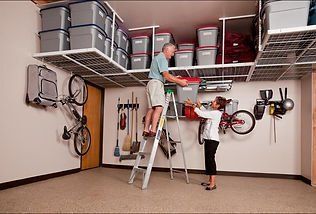Garage with overhead storage; person on ladder, another handing him a bin. Bikes on wall.