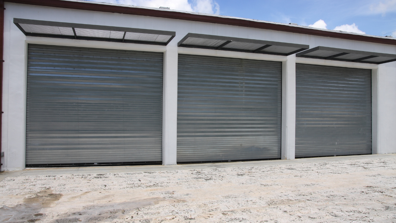 Three gray roller shutter doors on a white building, under a blue sky.