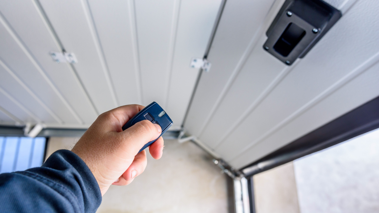 Hand pressing a garage door opener remote; door partially open.