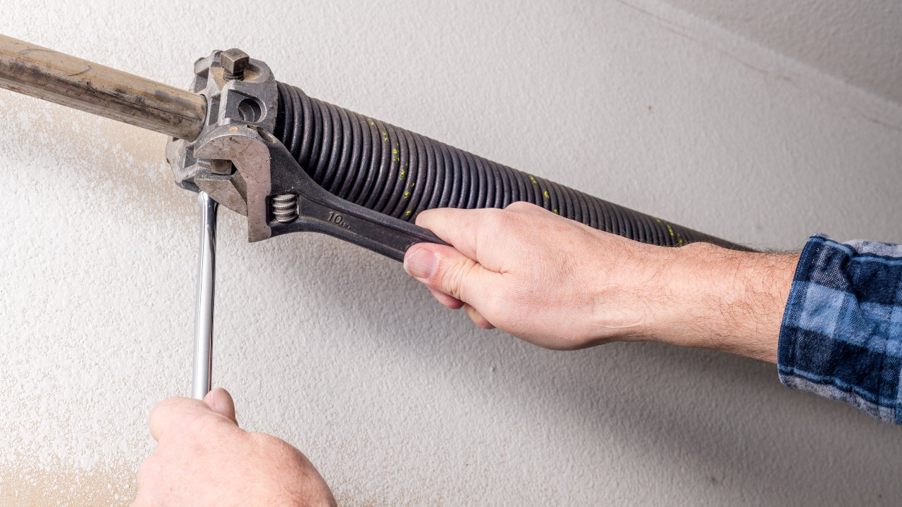 Person using a wrench and screwdriver to adjust a garage door spring, indoors.