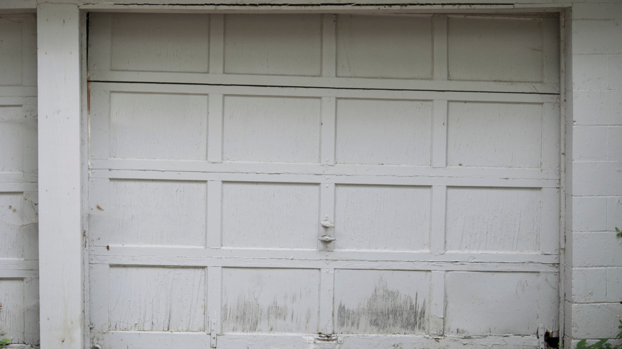 White, paneled garage door with weathered paint and visible lock.