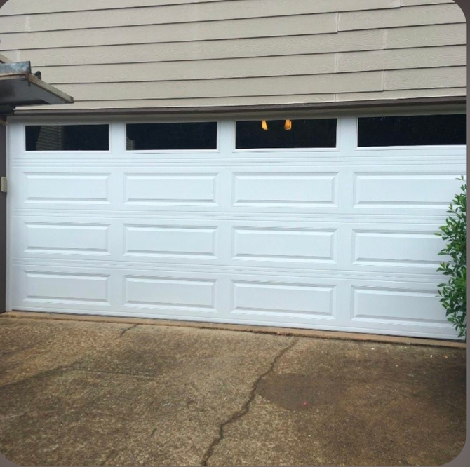 White garage door with small upper windows on a concrete driveway beside a house