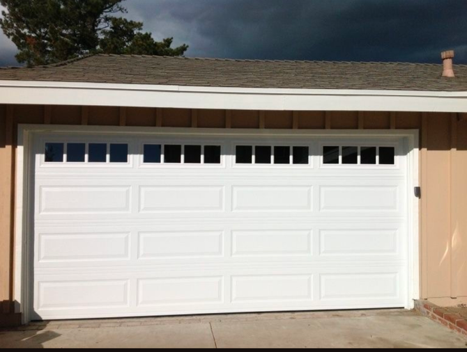 White two-car garage door on a beige house exterior under a cloudy sky.
