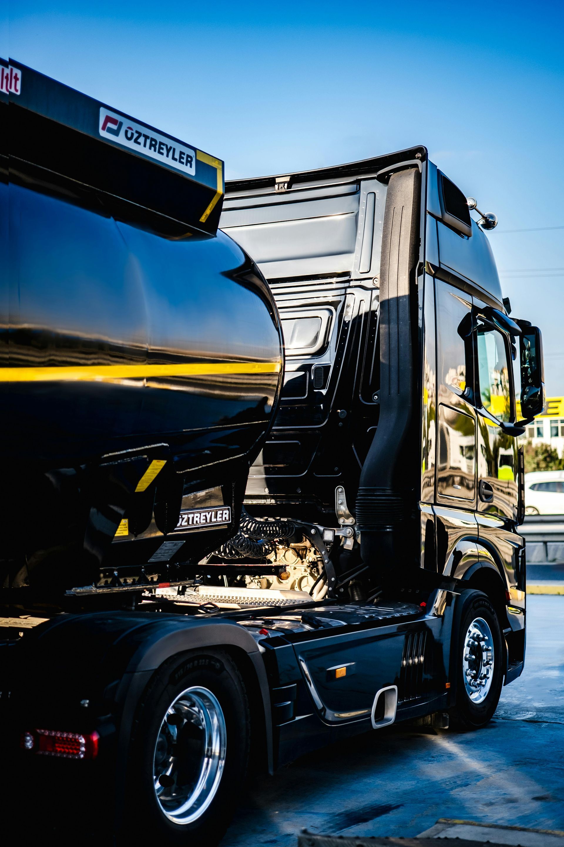 Black garbage truck at a loading site with crushed front cab and visible damage.