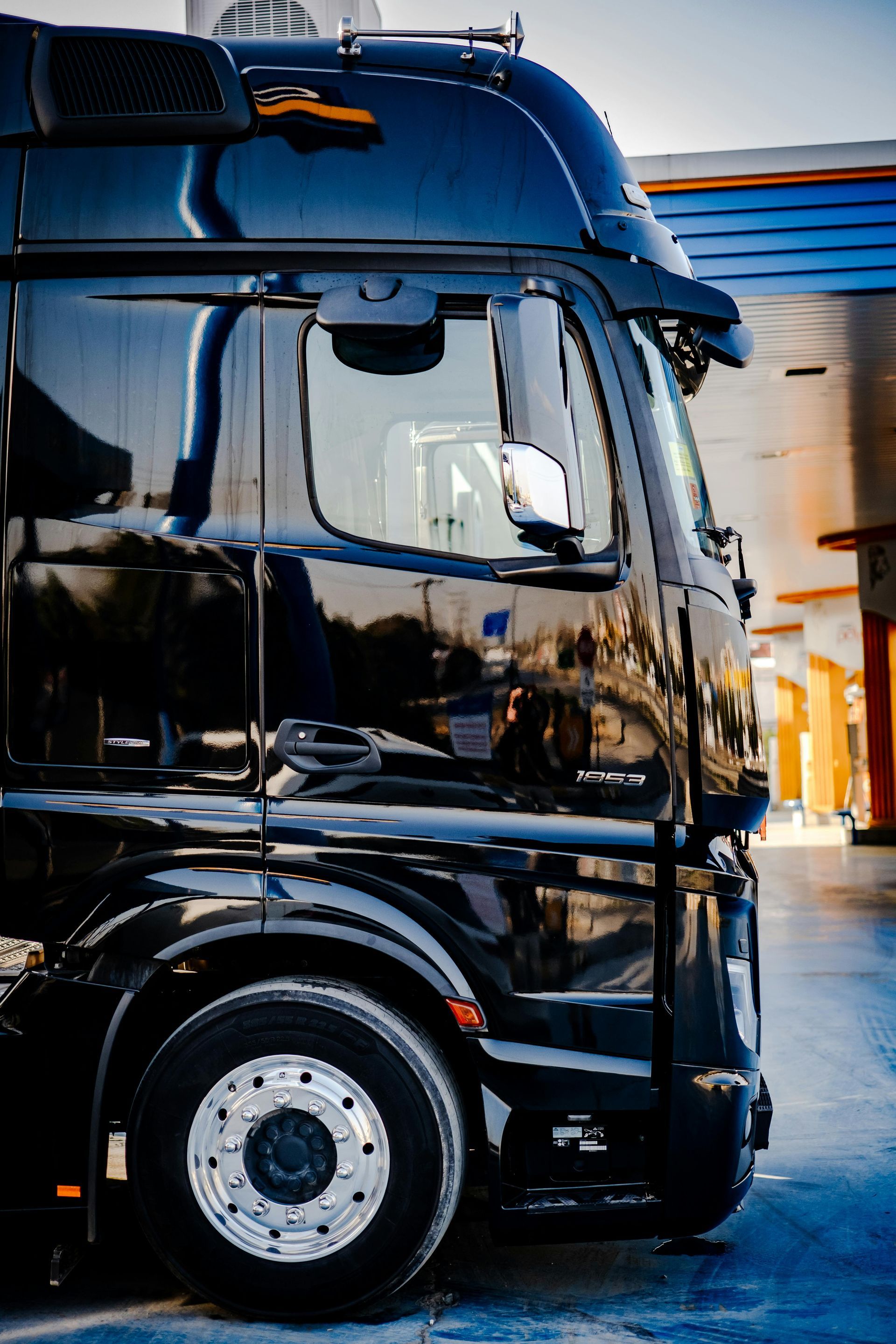Black semi-truck cab parked outdoors near a warehouse, with a glossy reflective finish
