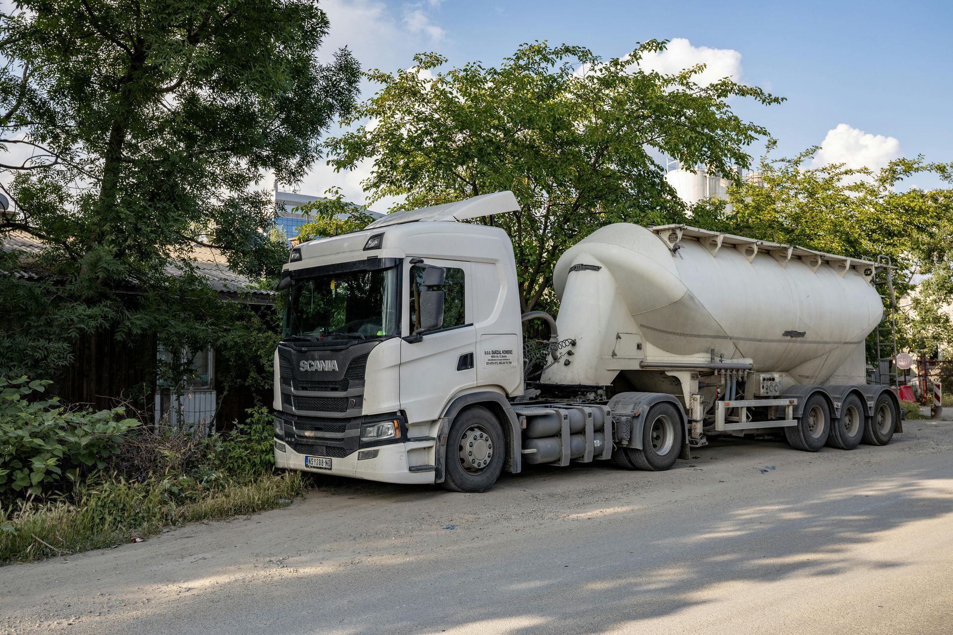 White cement mixer truck parked on a roadside beside trees and bushes