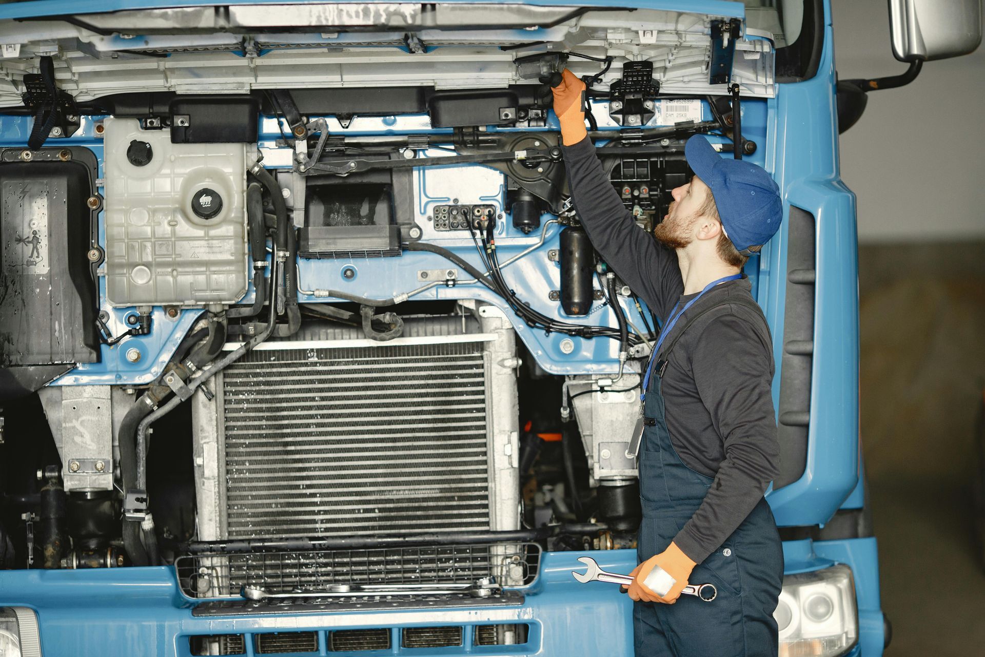 Mechanic inspecting the underside of a blue truck in a garage with the cab tilted forward