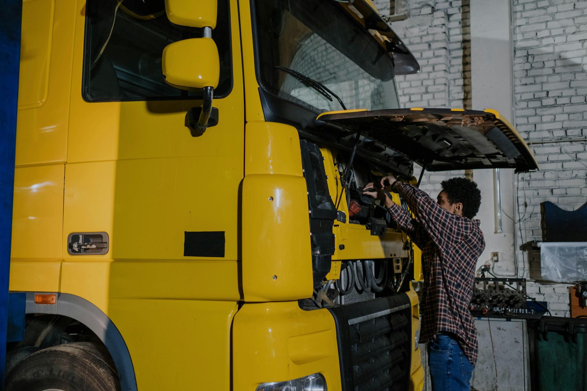 Mechanic working under the hood of a yellow truck inside a garage