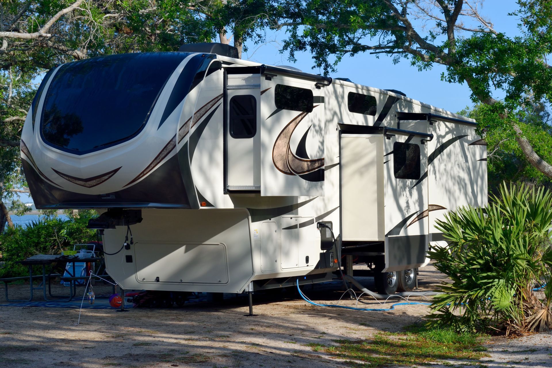 White and black RV trailer parked among trees on a sunny day