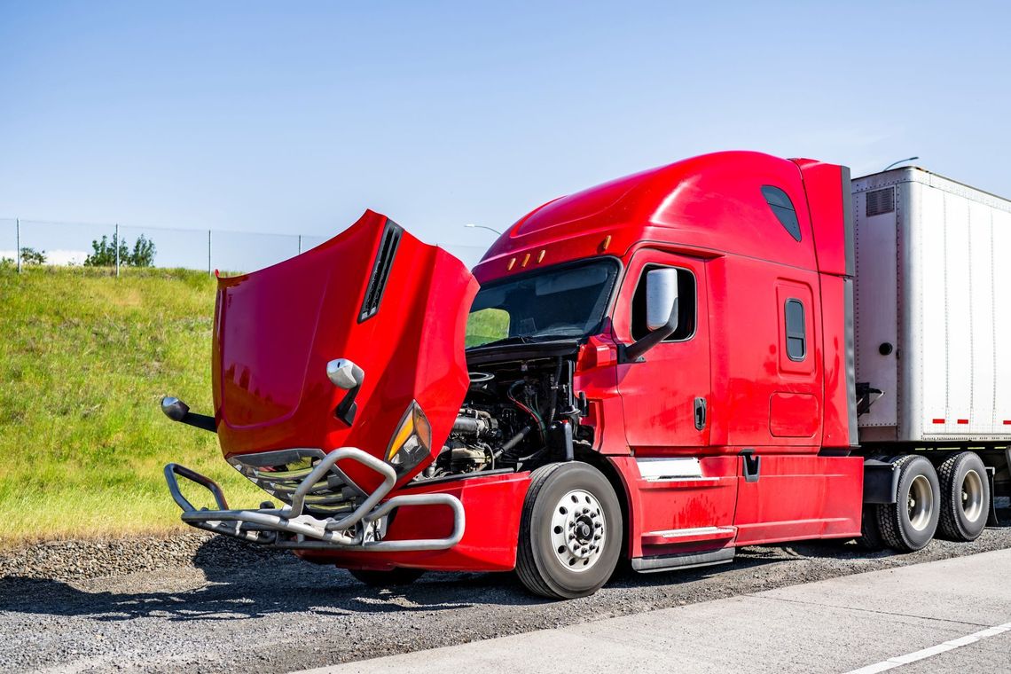 Red semi-truck with open hood parked on roadside, showing engine damage or inspection.