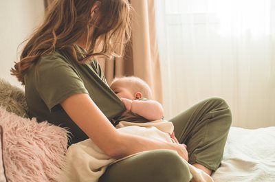 Person sitting on a bed, breastfeeding a baby in soft natural light