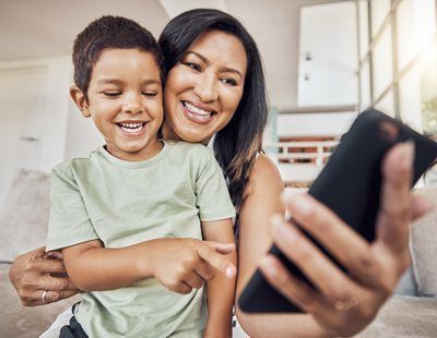Woman and child smiling at a phone screen indoors. Child points at screen.