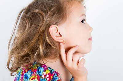 Girl with curly hair wearing earrings, touching her ear, against a white background.