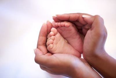 Hands cradling a baby's tiny feet, light skin, soft focus.