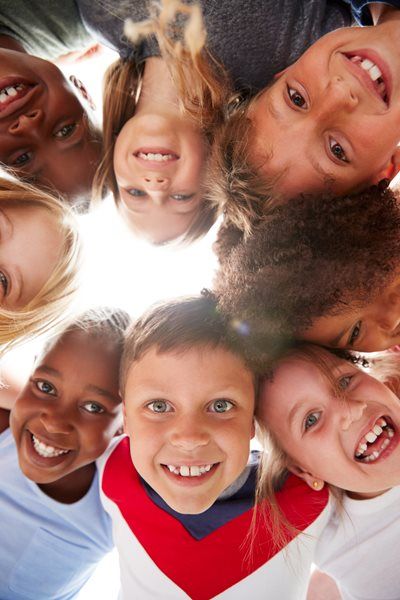Smiling children huddle together, looking down at the viewer from a sunny, outdoor perspective.
