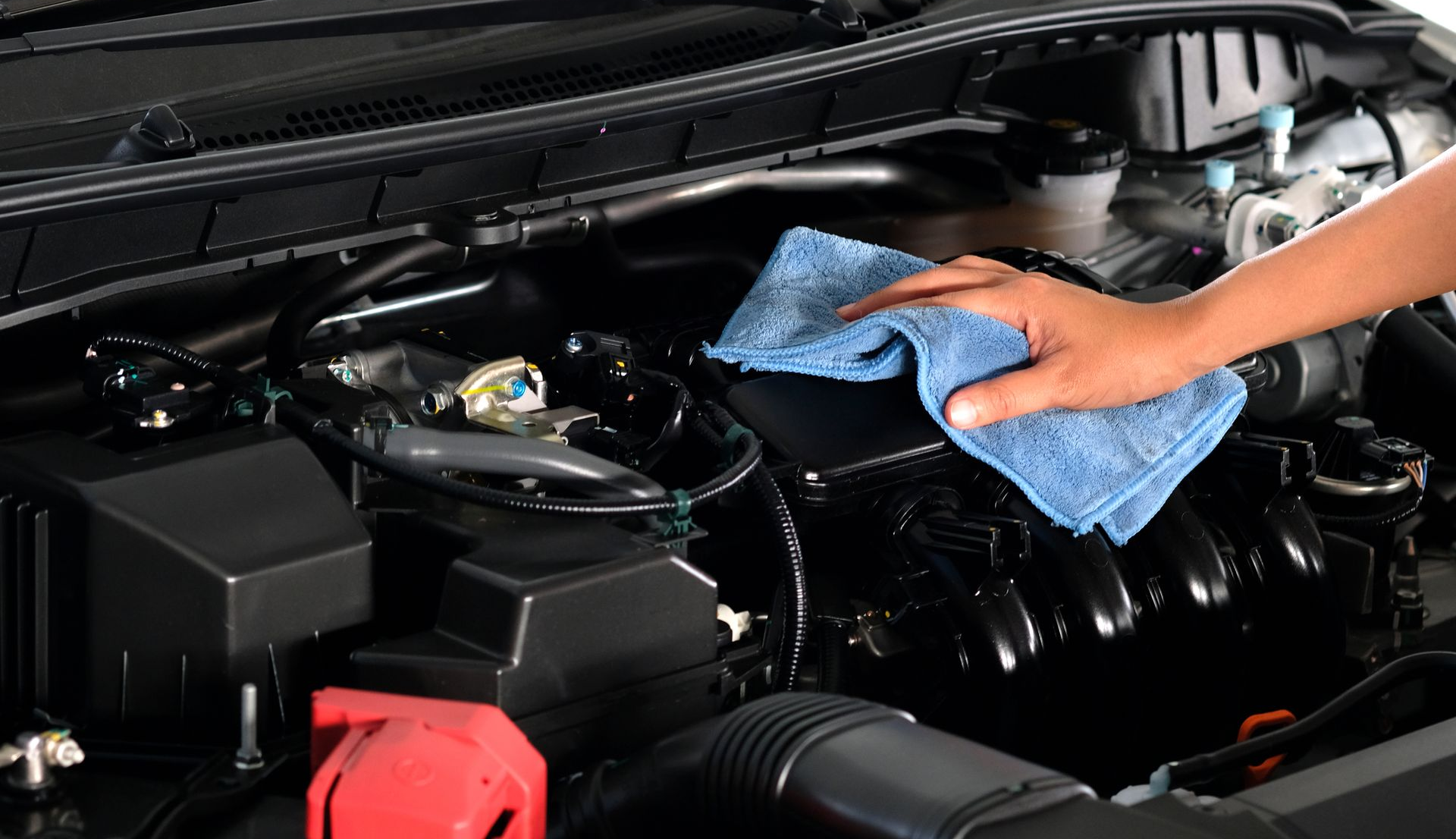 Hand wiping down a car engine with a blue microfiber cloth.