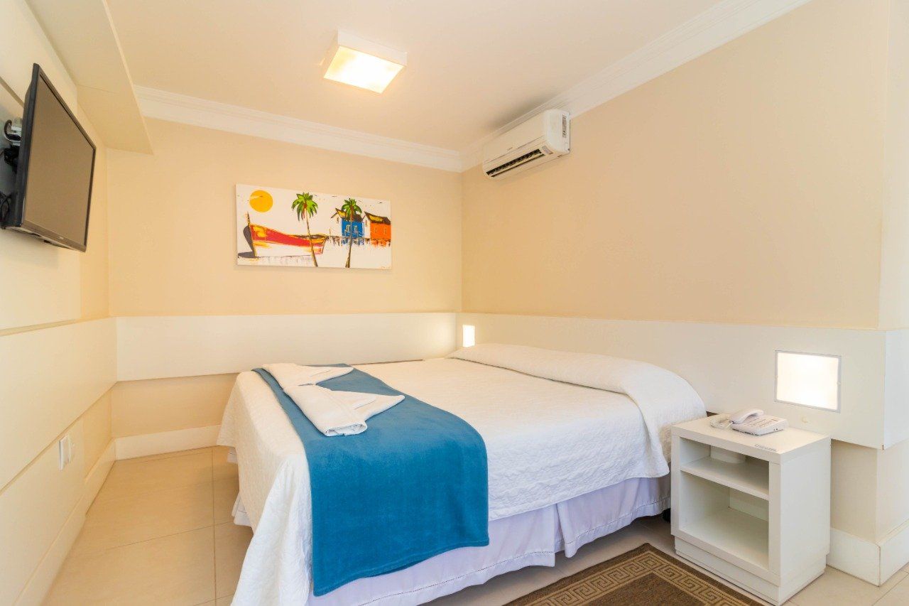 Um quarto de hotel com cama, mesa de cabeceira, televisão e ar condicionado.