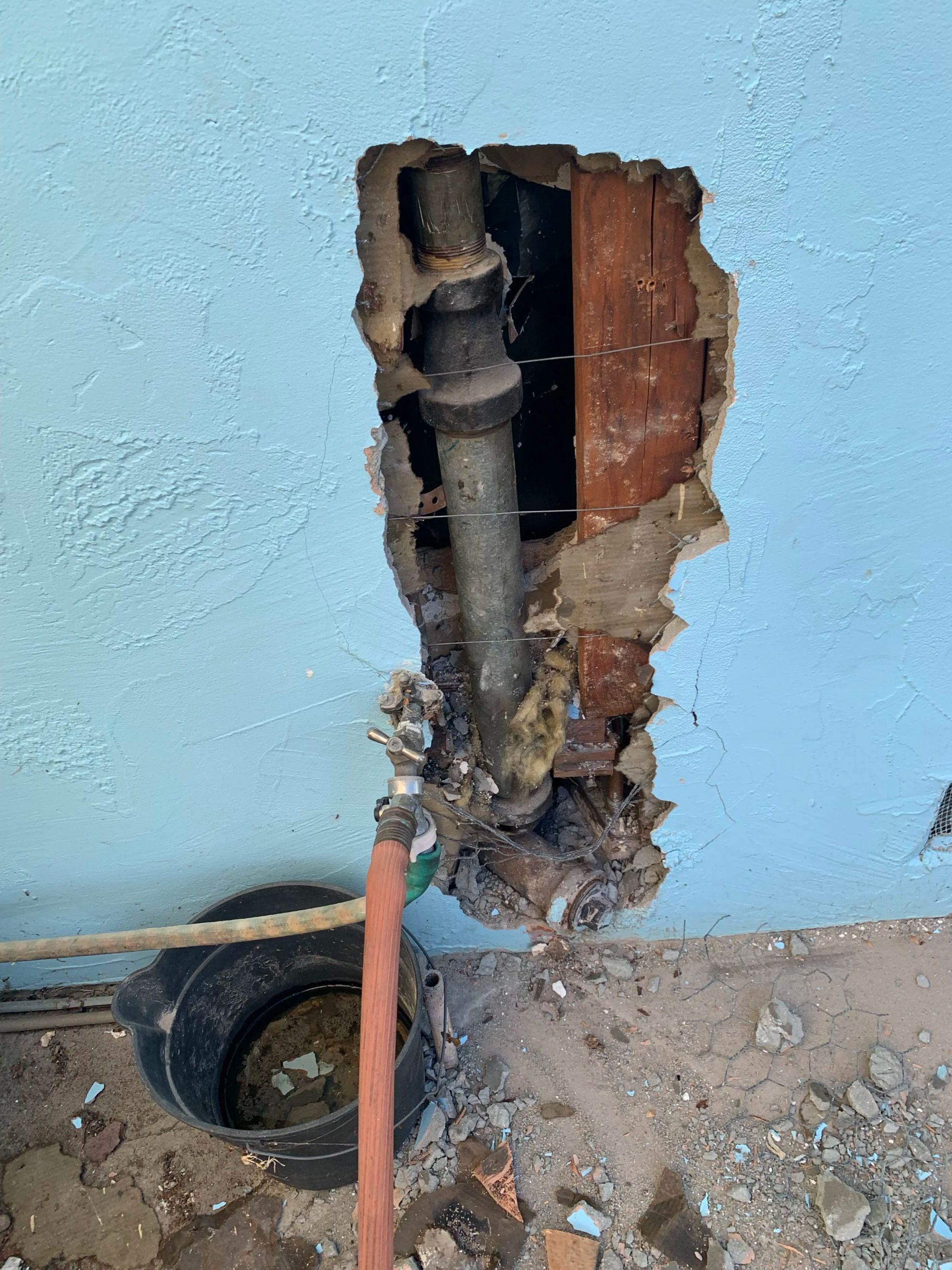 Damaged blue wall with exposed pipes and broken plaster near the floor