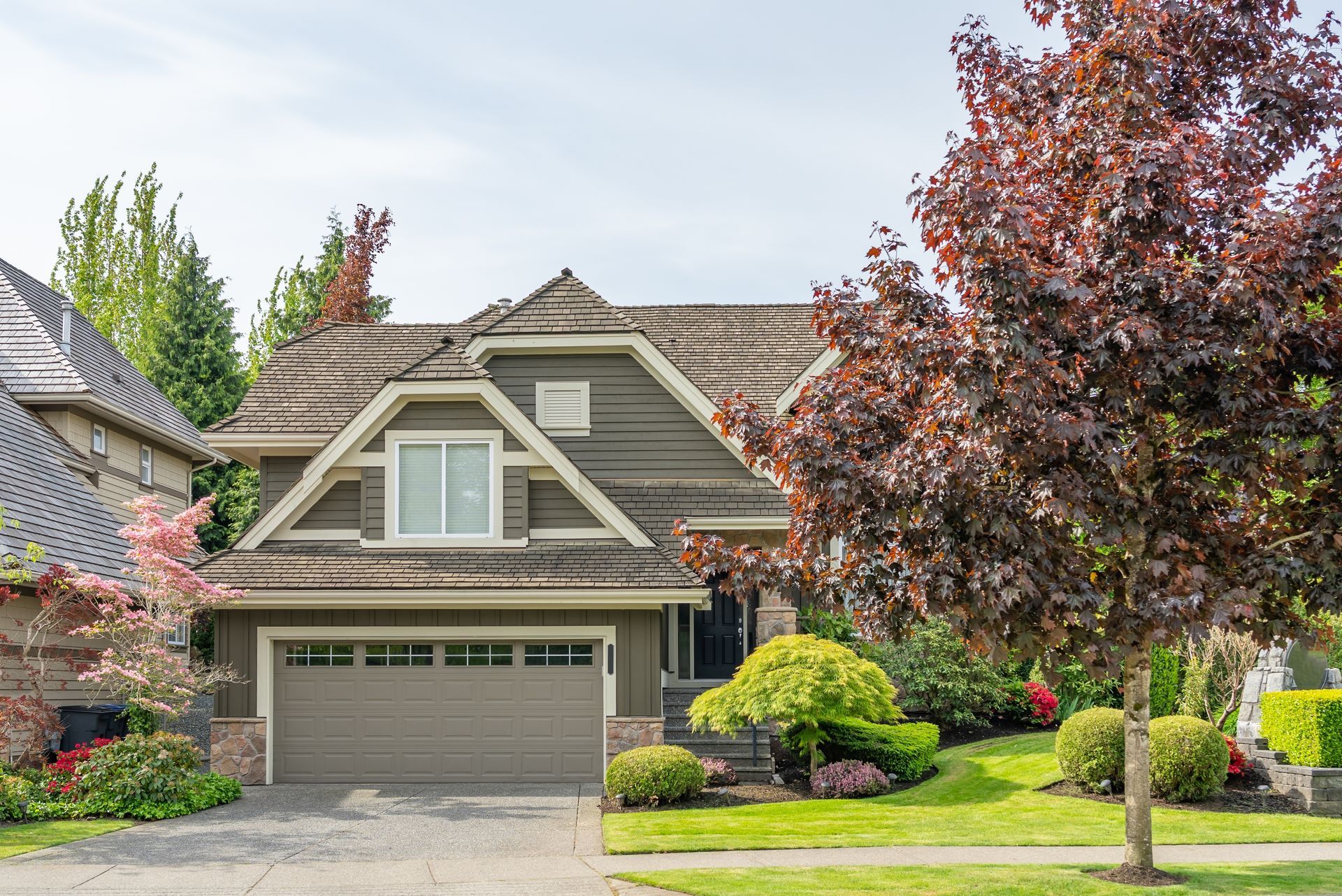 Suburban house with a two-car garage, green lawn, and a large tree in front
