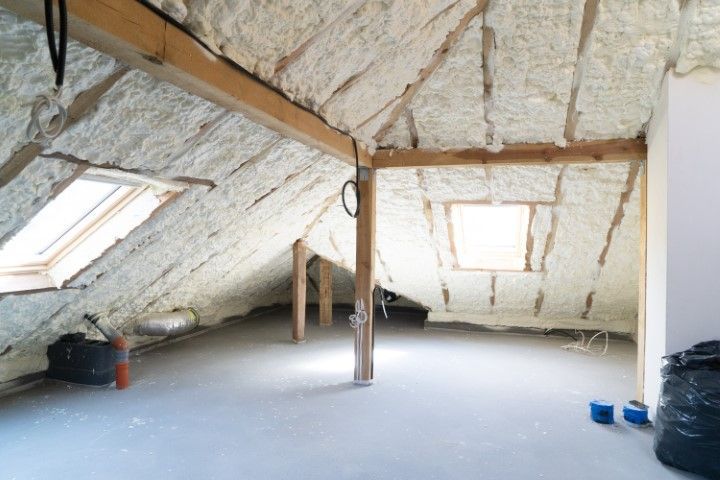 Attic space with spray foam insulation on the sloped roof and unfinished floor.
