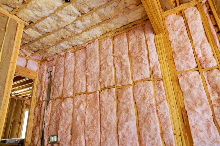 Interior of a building under construction, showing pink insulation between wooden beams.
