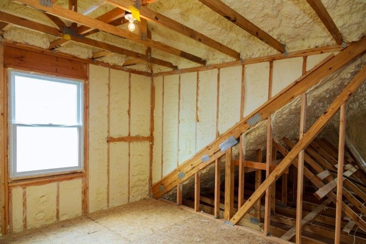 Attic interior, insulated with yellow foam, wooden beams, window, empty.