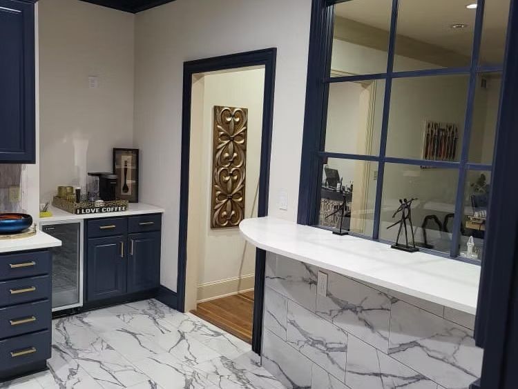 Modern kitchen with blue cabinets, white marble counters, and a large pass-through window.