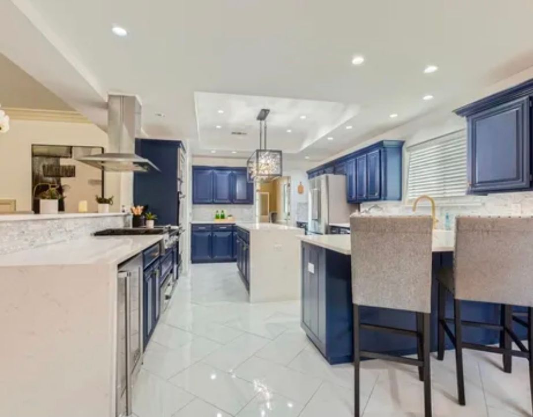 Bright modern kitchen with white tile floors, blue cabinets, island, and two barstools