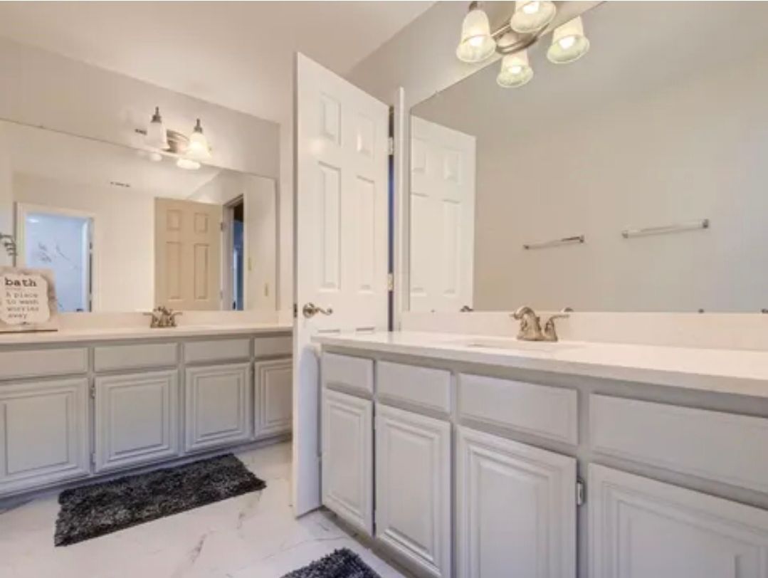 Bright bathroom with double vanity, large mirror, white cabinetry, and soft lighting
