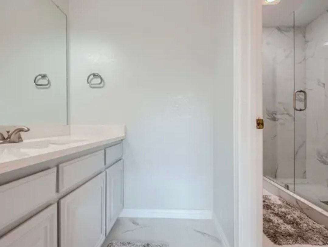Modern bathroom with white vanity, mirror, and glass shower doors with marble tile.