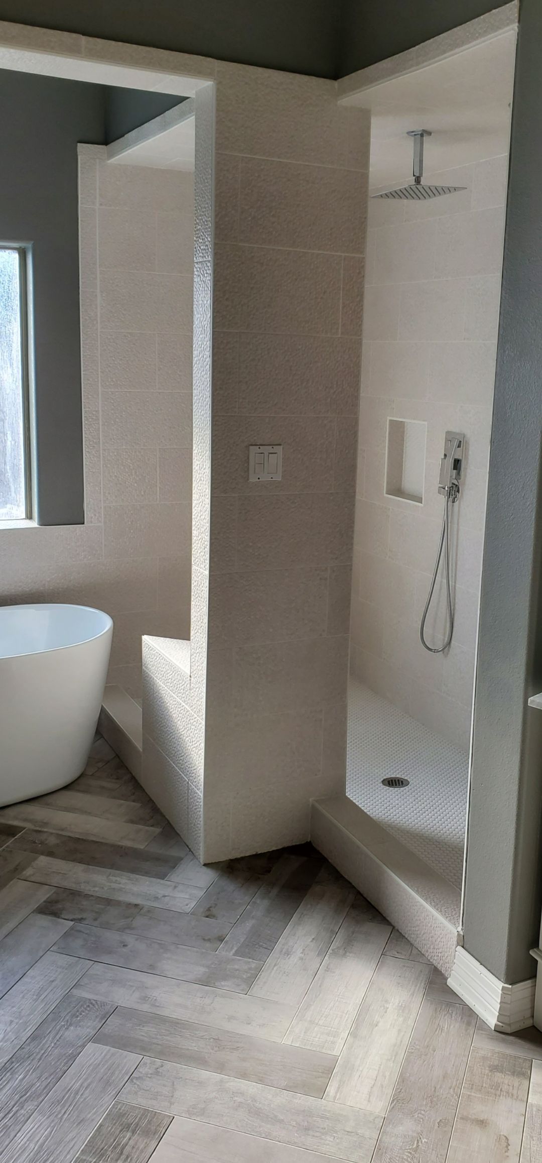 Modern bathroom with walk-in shower, white tub, and gray herringbone tile floor.
