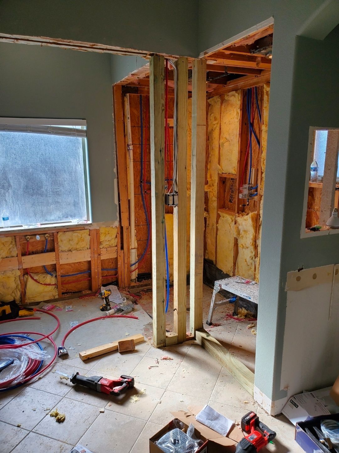 Partially gutted room under renovation with exposed studs, insulation, tools, and debris on the floor