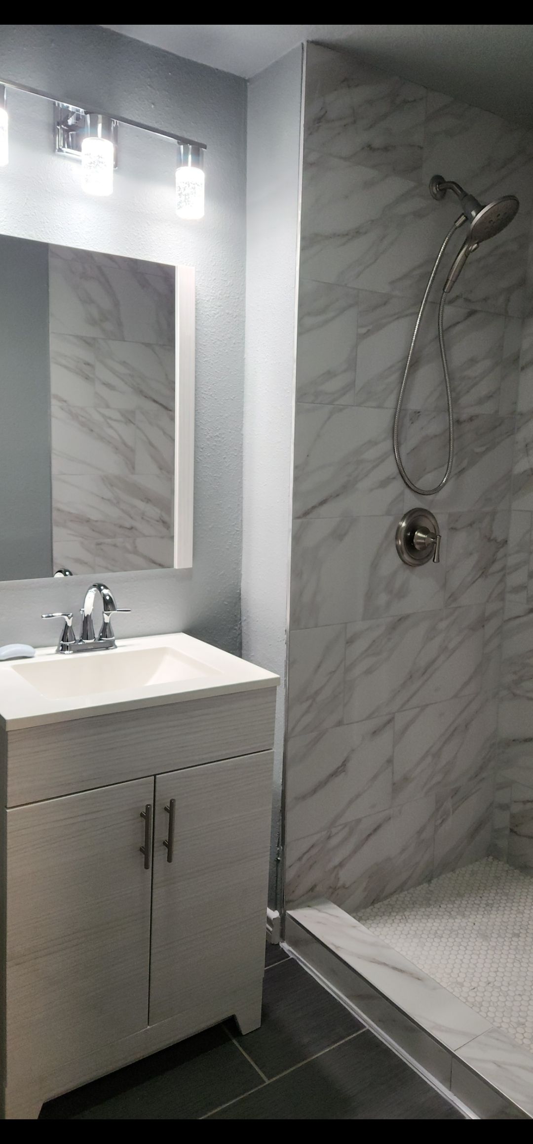 Small modern bathroom with white vanity, mirror, and marble-tiled shower with chrome fixtures