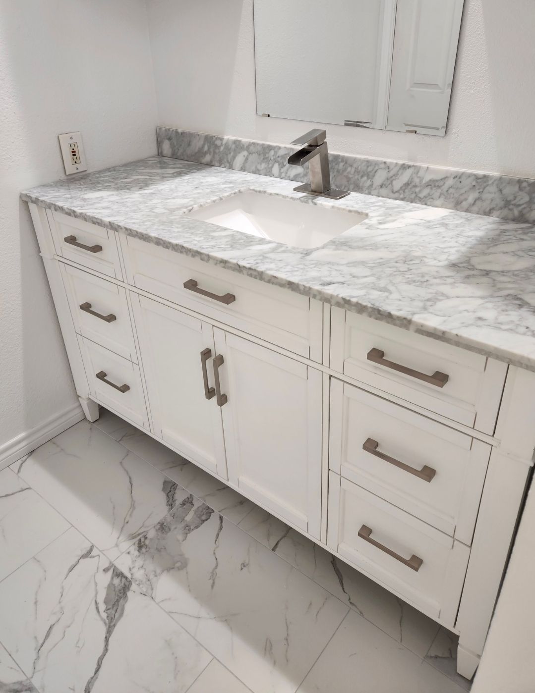 White bathroom vanity with marble countertop, chrome faucet, and tiled floor under a window