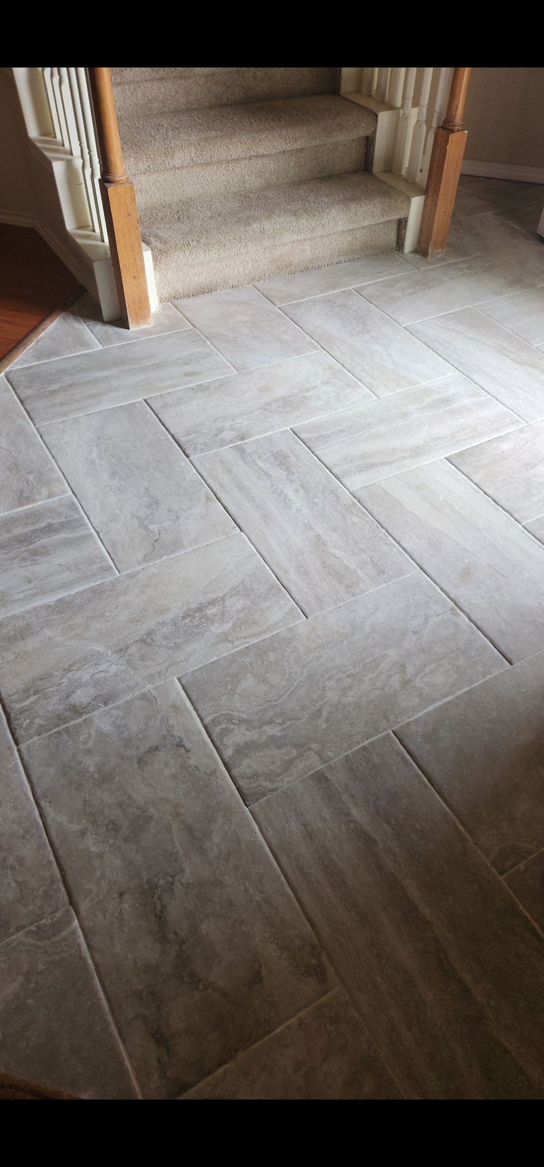 Gray herringbone floor leading to a carpeted staircase with wooden trim