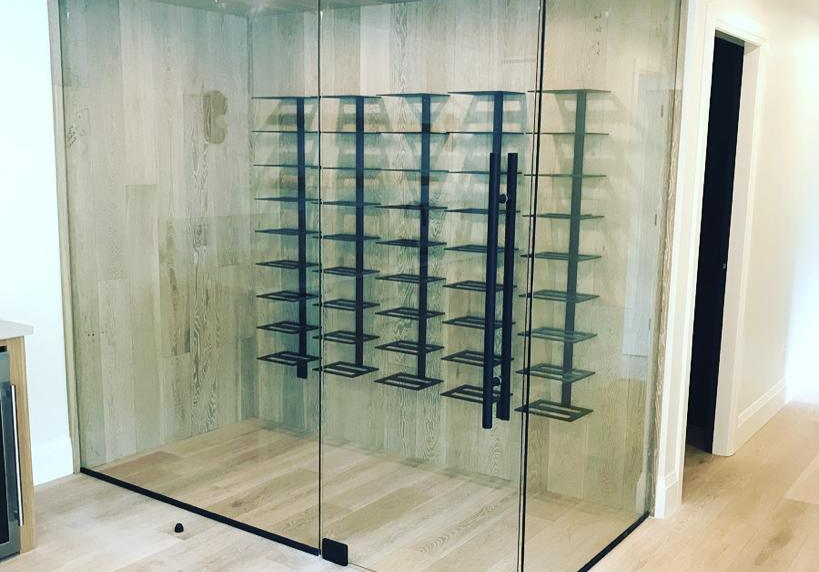 A wine cellar with a glass door and shelves filled with wine bottles.