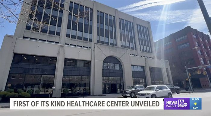 Exterior view of a light-colored healthcare center building with an arched entrance on a sunny day.
