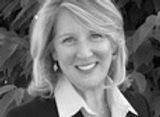 Woman with blonde hair smiling, wearing a blazer and button-up shirt, outdoors.