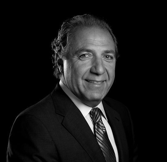 Man in a suit smiles, dark background.