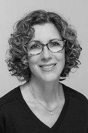 Woman with curly hair and glasses smiling at the camera, wearing a dark sweater.