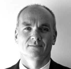 Man in a suit, looking at the camera, with a neutral expression. Black and white photo.
