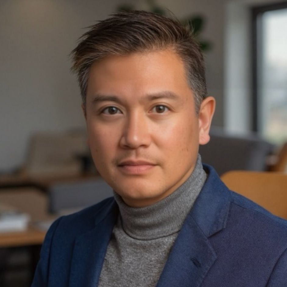 Man wearing a gray turtleneck and blue blazer looking directly at the camera, indoors.