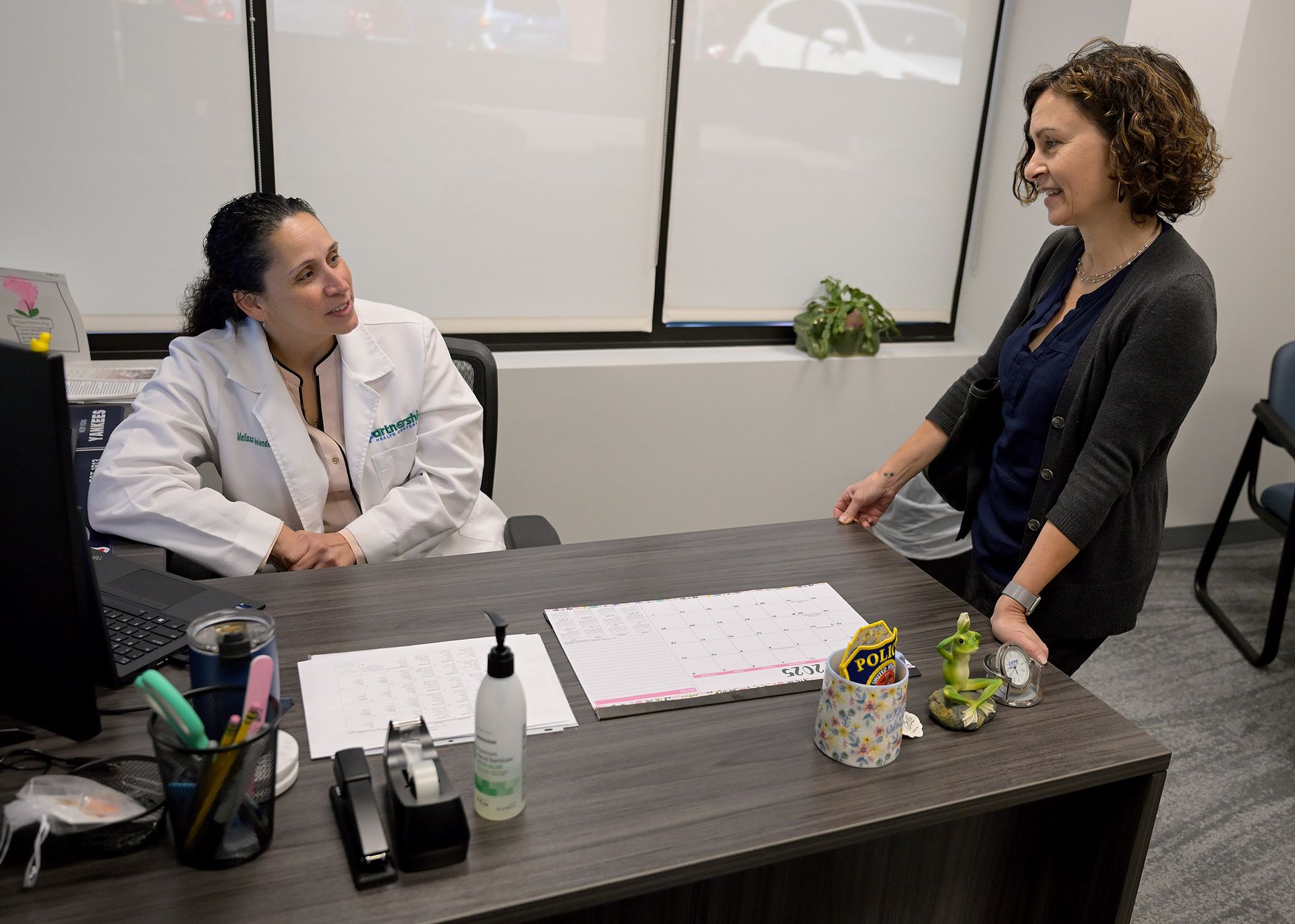Doctor in white coat consults with patient in office; both are smiling.