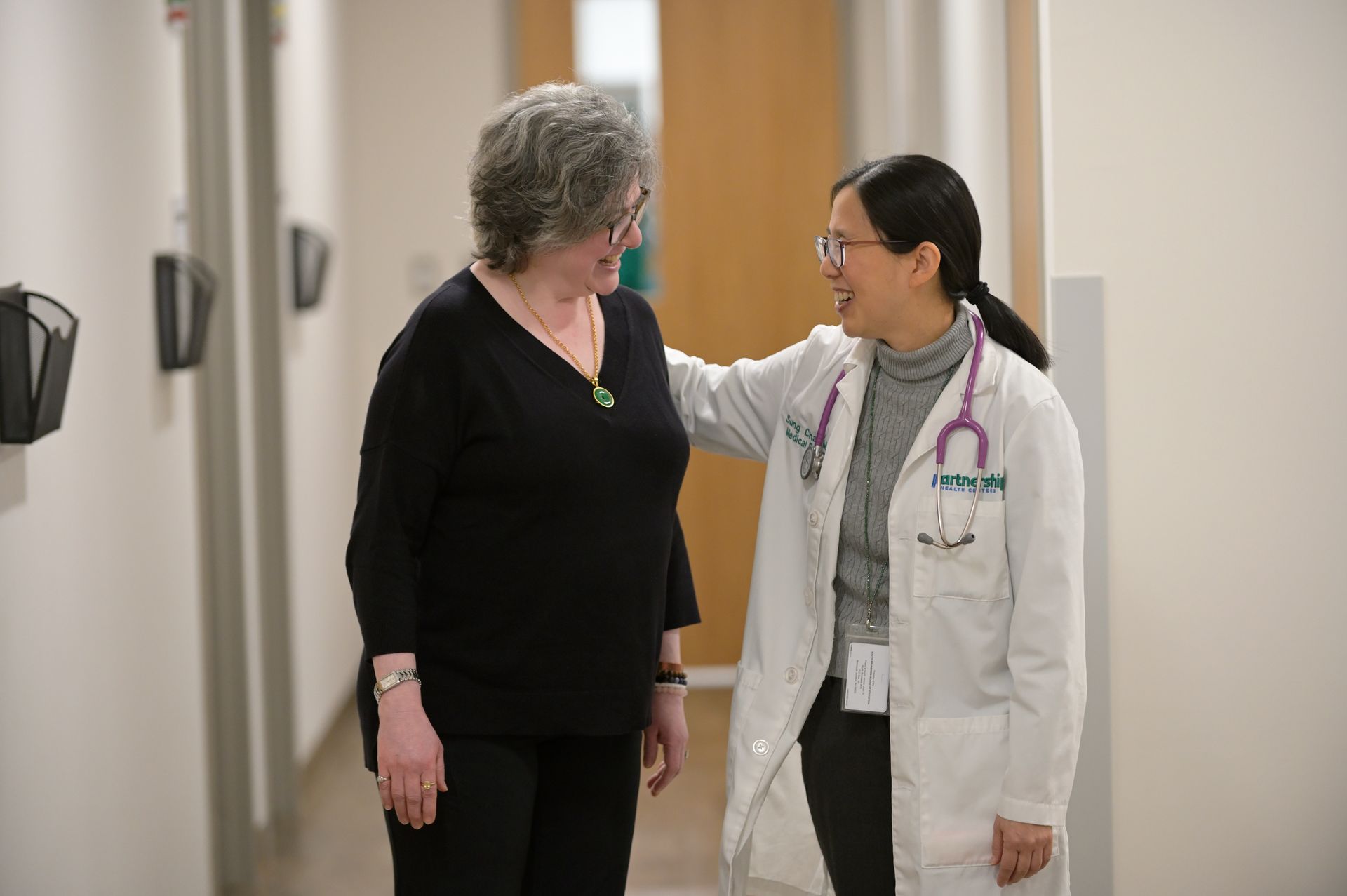 Doctor and patient smiling in a hallway; doctor's arm on patient's shoulder.