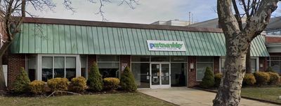 Exterior of a Petco store with green signage, red brick, and shrubs.
