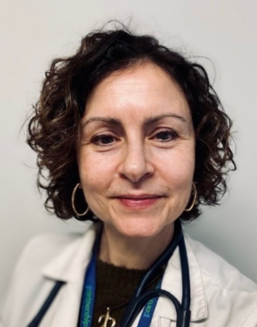 Woman with curly brown hair, wearing a white coat and stethoscope.