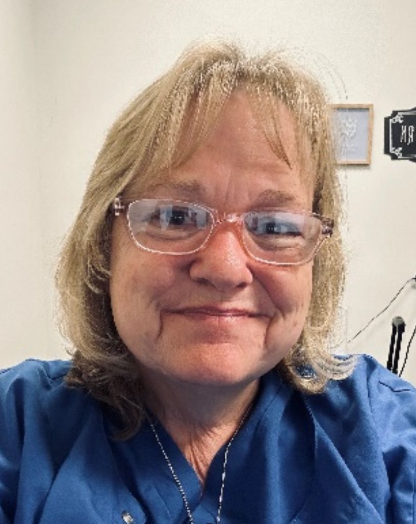 Woman with glasses smiles at the camera, wearing a blue shirt.