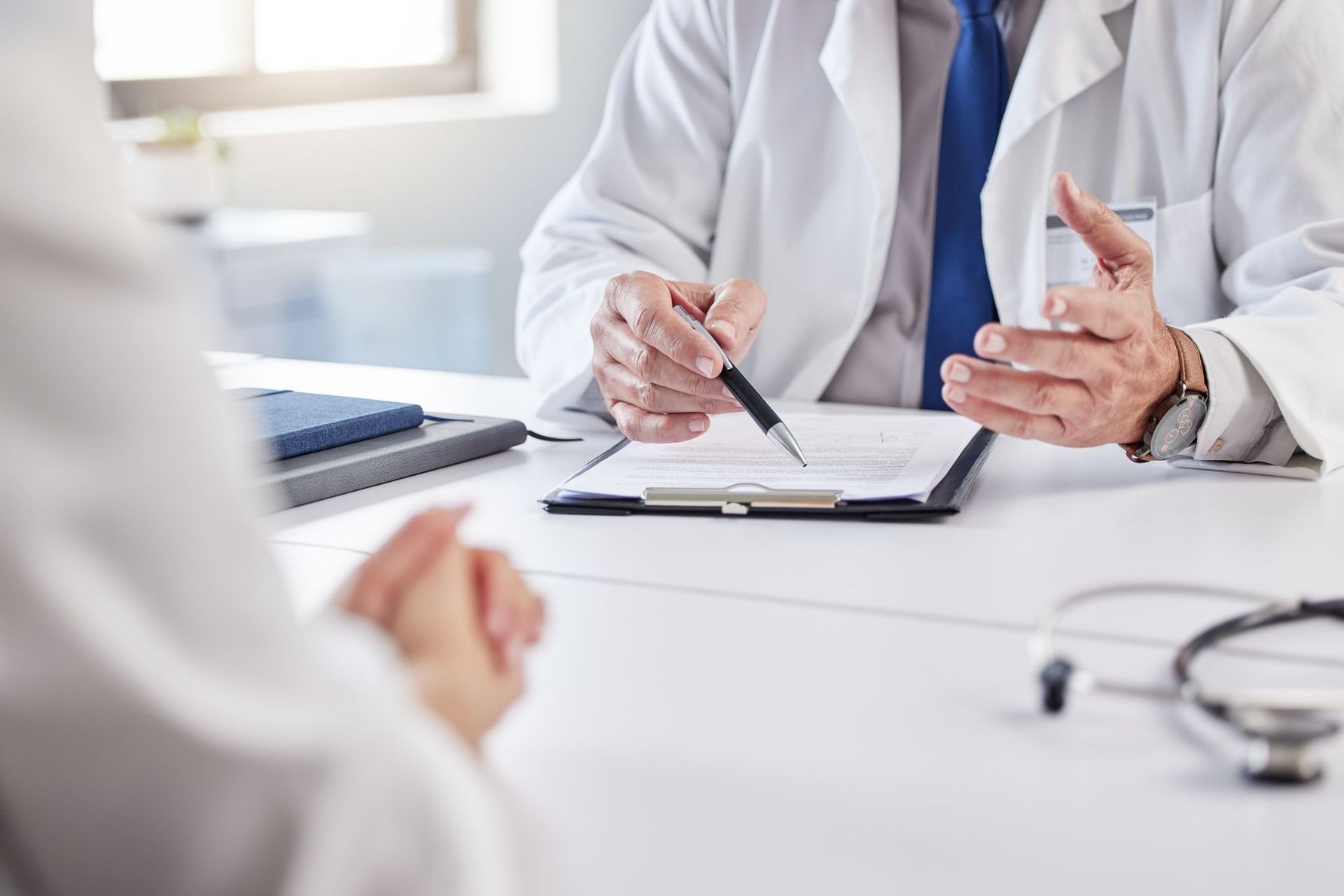 Doctor pointing at chart, explaining to a patient in a medical office setting.