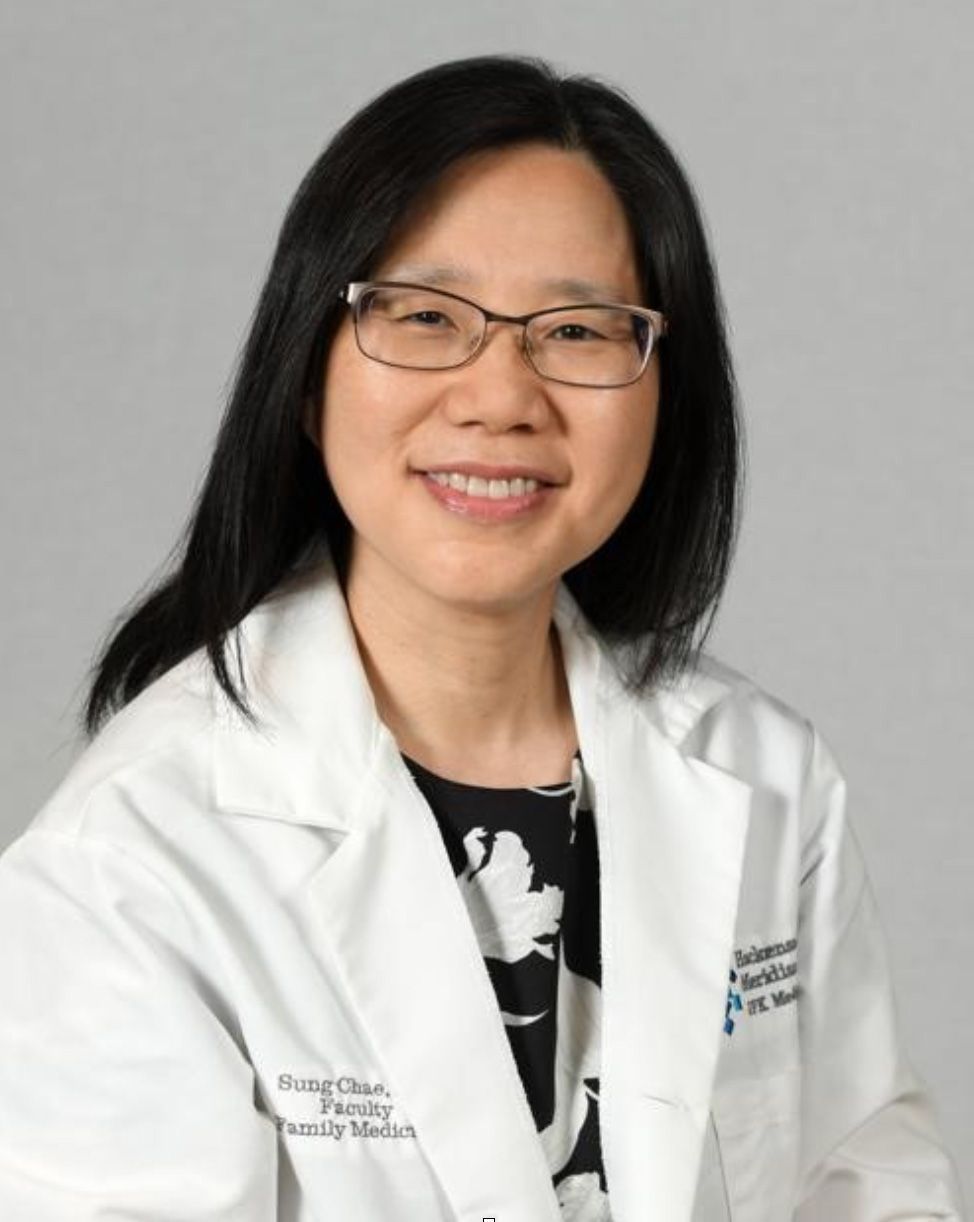 Woman in glasses and white coat, smiling, professional headshot.