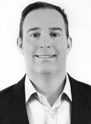 Man in suit jacket smiles at the camera, head and shoulders, black and white photo.